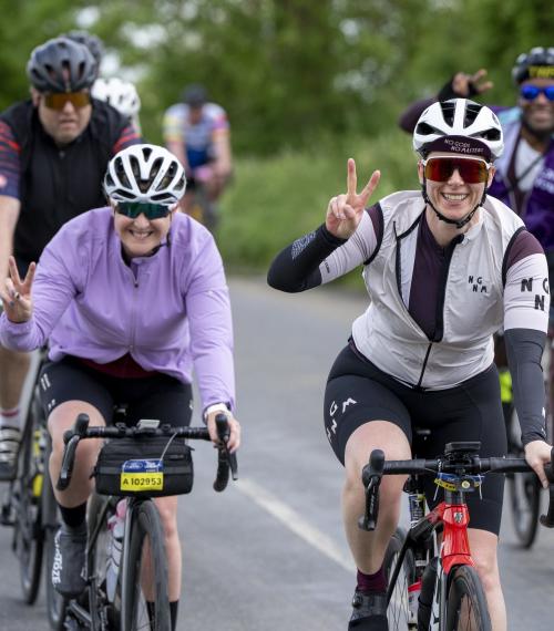 Two woman cycling in the RideLondon event make the peace sign